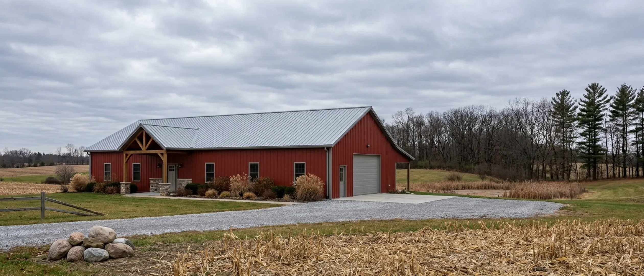 A completed barndominium with a covered entry porch and an attached shop bay, photographed in flat overcast late-autumn daylight.